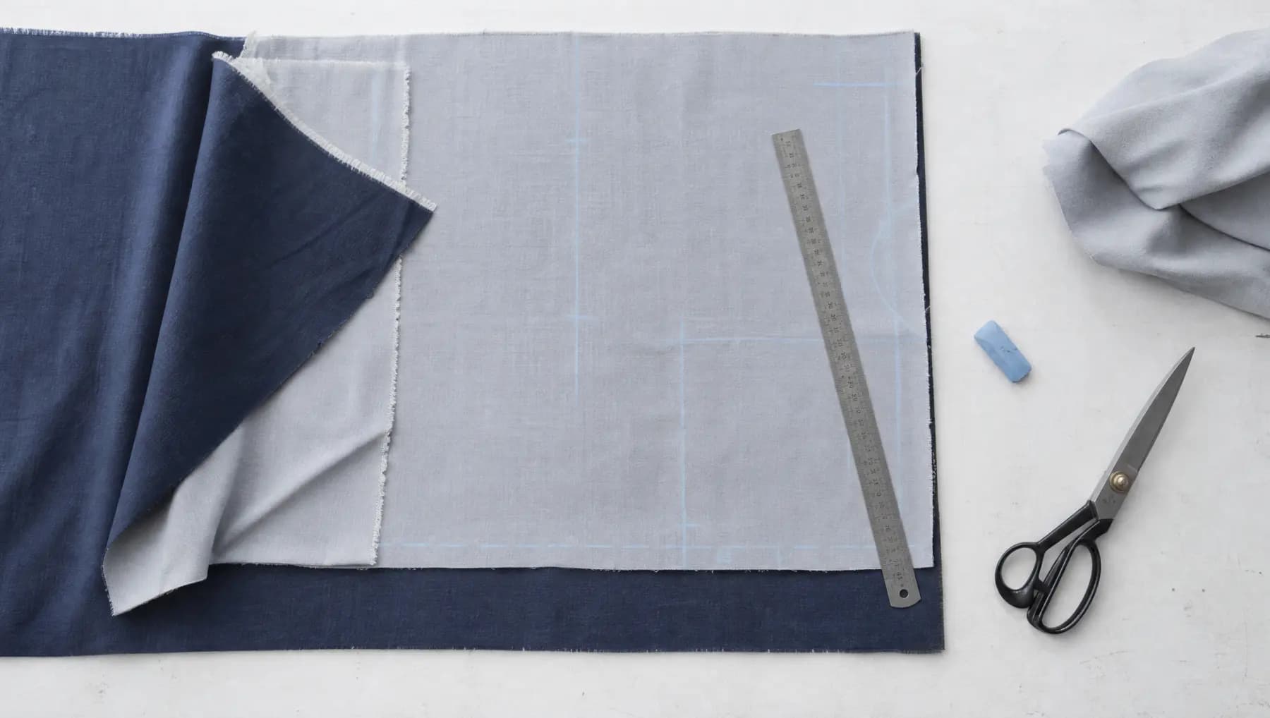 A cutting table seen from above with layered fabric panels, a steel rule and chalk-blue marking lines.