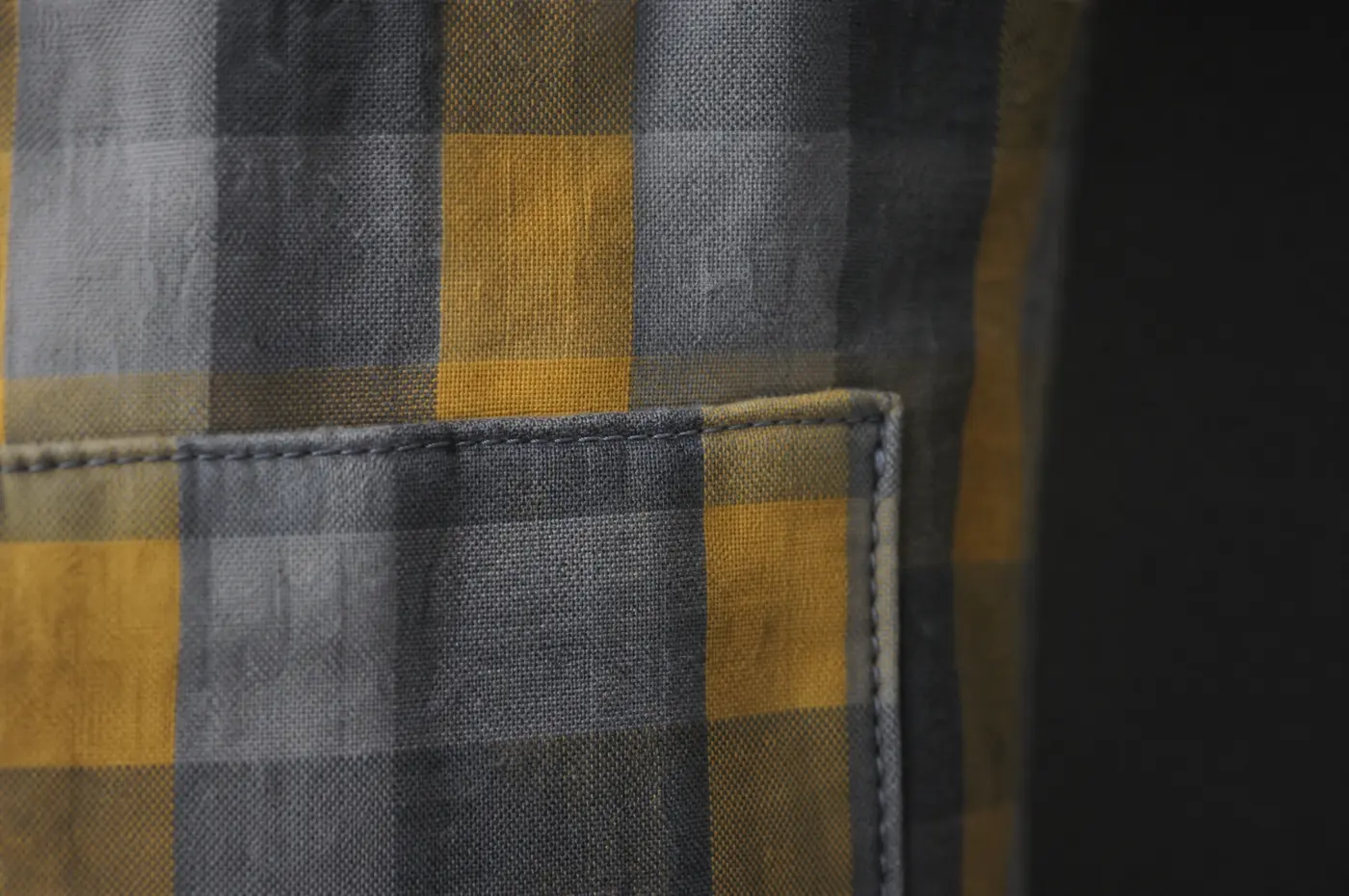 A checked fabric where the pattern meets a pocket seam, photographed close up under raking light.