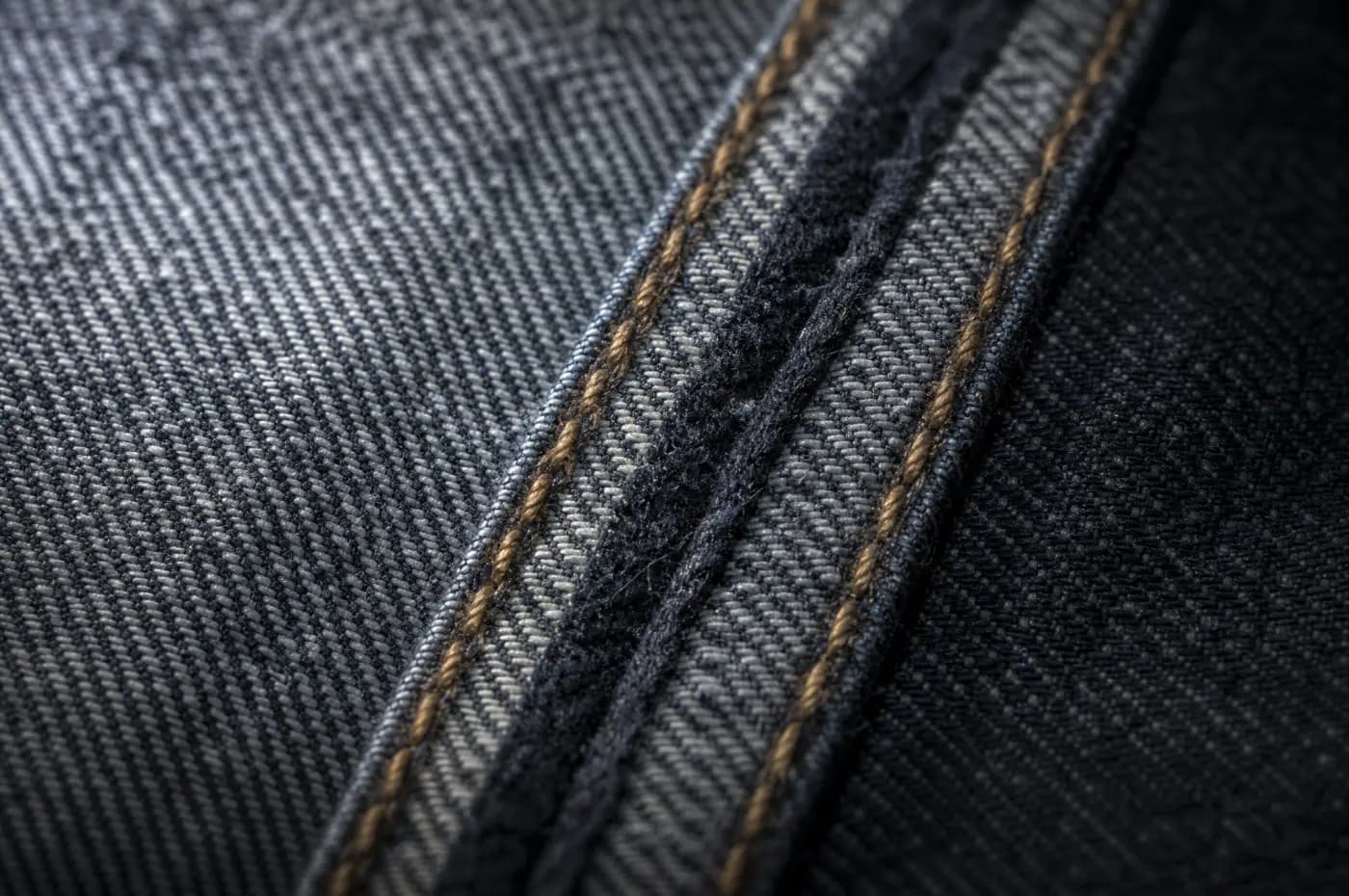 Two parallel rows of stitching enclosing the edge of a denim seam.