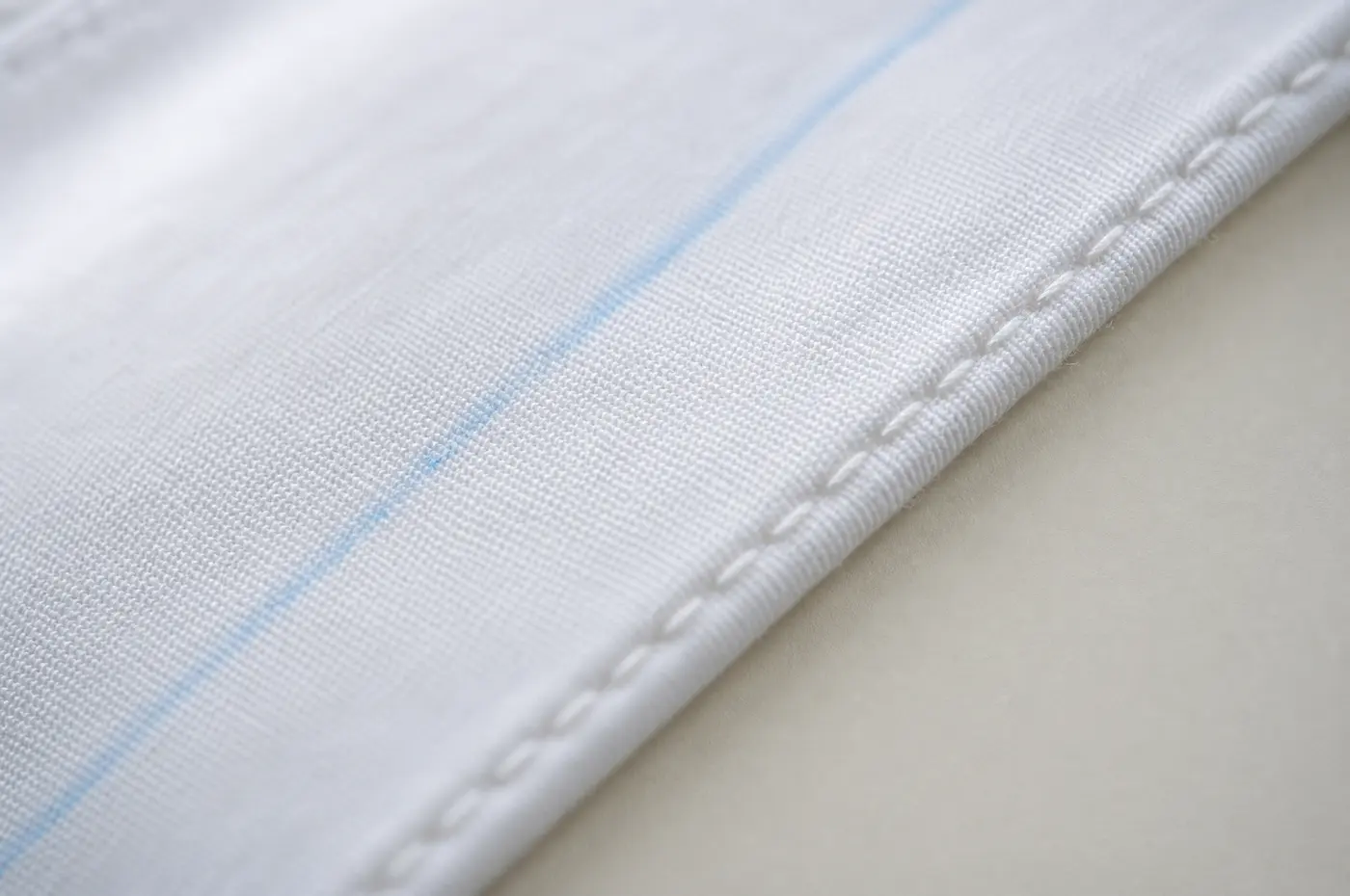 A narrow folded seam on white cotton with the raw edge enclosed inside it.